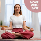 A lifestyle photo of a woman sitting cross-legged in a yoga pose on a grey rug, eyes closed with a peaceful expression. She wears a white cropped t-shirt and pink trousers. A pink circle in the top-right corner features the white text 'MOVE WITH EASE'.