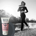 A promotional image for Below the Belt for Women Chafe Cream. In a black-and-white background, a woman in athletic wear is jogging alongside a river at sunset. In the foreground, a full-color 75ml tube of the Fresh Breeze anti-chafe cream is prominently displayed.