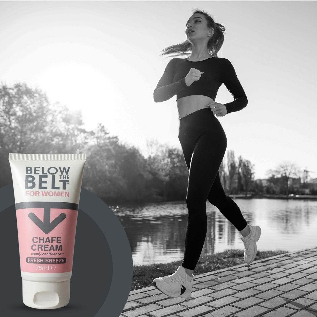 A promotional image for Below the Belt for Women Chafe Cream. In a black-and-white background, a woman in athletic wear is jogging alongside a river at sunset. In the foreground, a full-color 75ml tube of the Fresh Breeze anti-chafe cream is prominently displayed.