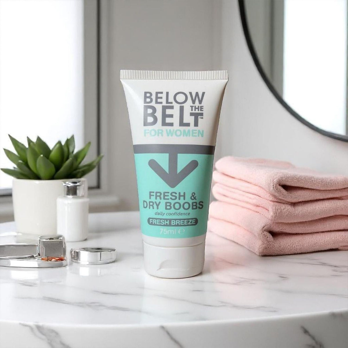 The 75ml tube is displayed on a white marble countertop next to a stack of pink towels and a small potted plant in a bright, modern bathroom setting