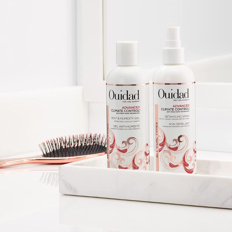 Two bottles of Ouidad hair care products on a white surface with a brush in the background.
