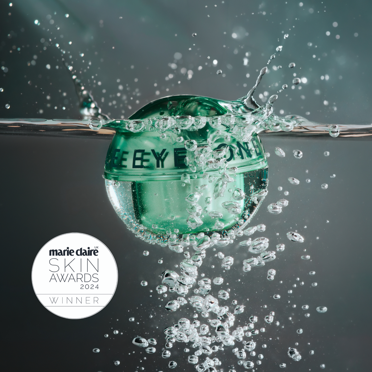 A translucent green cosmetic jar floating in splashing water on a dark gray background, with a white circular Marie Claire Skin Awards 2024 Winner badge in the lower left.