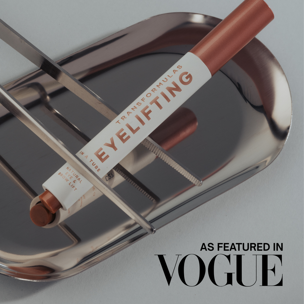 An eye makeup tube labeled 'TRANSFORMFORMULAS EYELIFTING' resting on a reflective silver metal tray, with 'AS FEATURED IN VOGUE' text in the lower right corner.