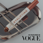 An eye makeup tube labeled 'TRANSFORMFORMULAS EYELIFTING' resting on a reflective silver metal tray, with 'AS FEATURED IN VOGUE' text in the lower right corner.