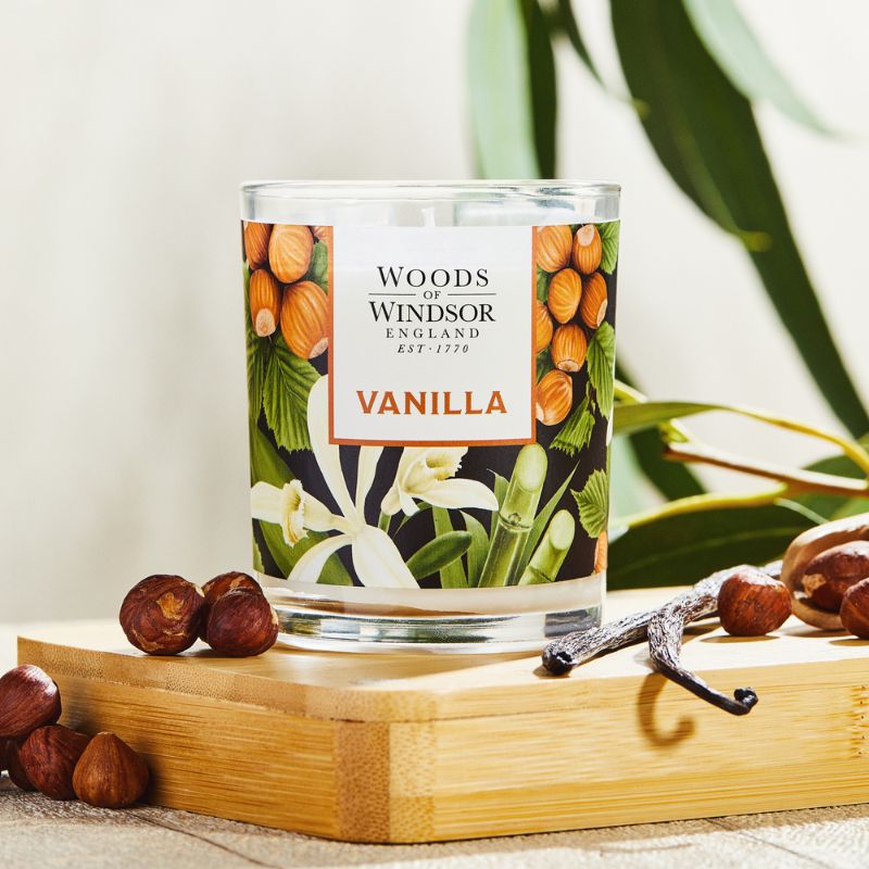 Candle with vanilla pods next to it on a bamboo board.