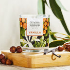 Candle with vanilla pods next to it on a bamboo board.